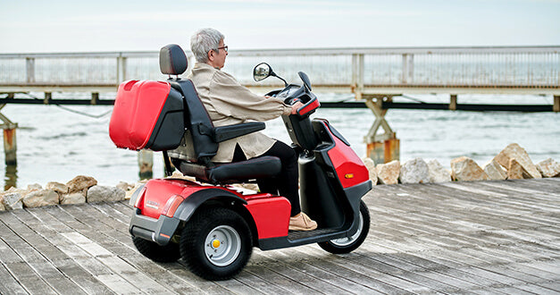AFIKIM Red Afiscooter S3 Outdoor Mobility Scooter with Rider on Seaside, Side View
