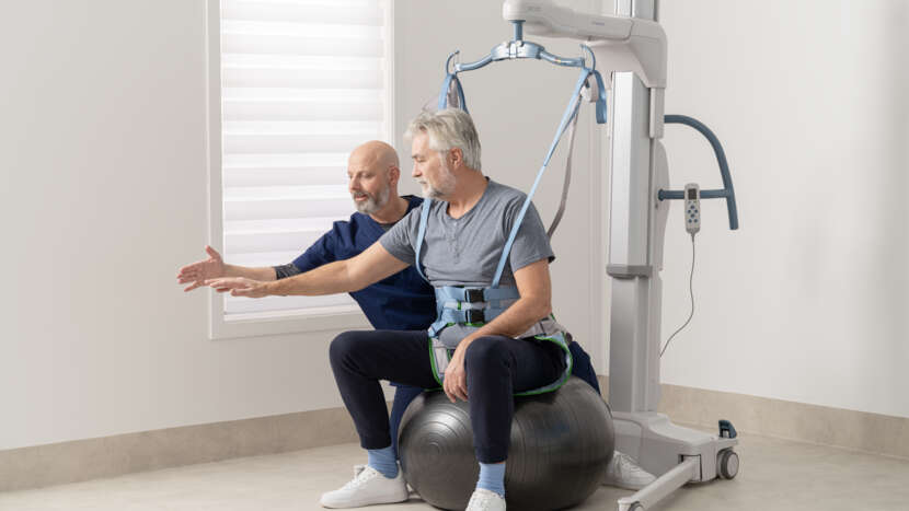 Arjo Maxi Move 5 Multifunctional Powered Patient Floor Lift With Patient And Caregiver In Rehabilitation Use View