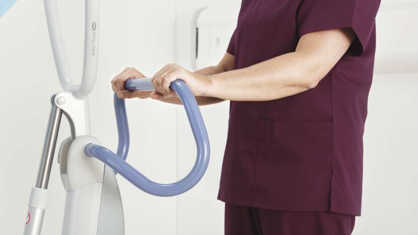 Arjo Sara Flex Sit to Stand Lift With Caregiver Holding Ergonomic Handlebar View