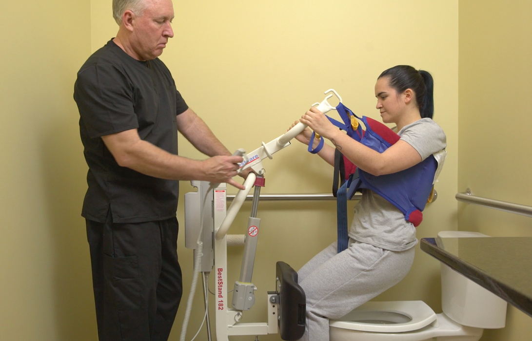 Bestcare BestStand SA228 Sit-to-Stand Patient Lift With Caregiver And Patient In Bathroom Transfer
