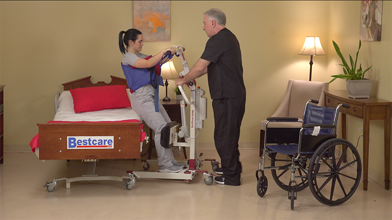 Bestcare BestStand SA400HE Mini Electric Sit-to-Stand Lift With Caregiver And Patient In Bedroom Transfer