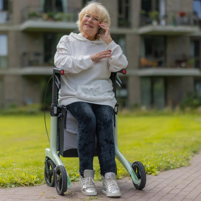 Rollz Air Carbon Rollator In Mint Green With A User Comfortably Seated On It.