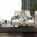 A mannequin dressed in a light green pajama set reclining on a Starsleep Orin Arlo ergonomic rotating chair bed with a remote control, set in a modern living room environment with a window, curtains, and a plant.
