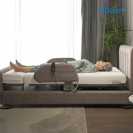 An elderly woman lies on aStarsleep Orin Arlo ergonomic rotating chair bed with a brown headboard and side rails in a modern bedroom setting. The brand logo 'Ari' by 'Bed & Bad' is visible in the top right corner.