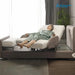 A woman relaxes in a Starsleep Orin Arlo ergonomic rotating chair bed, styled in a bright, contemporary room with a window, curtains, and a potted plant.